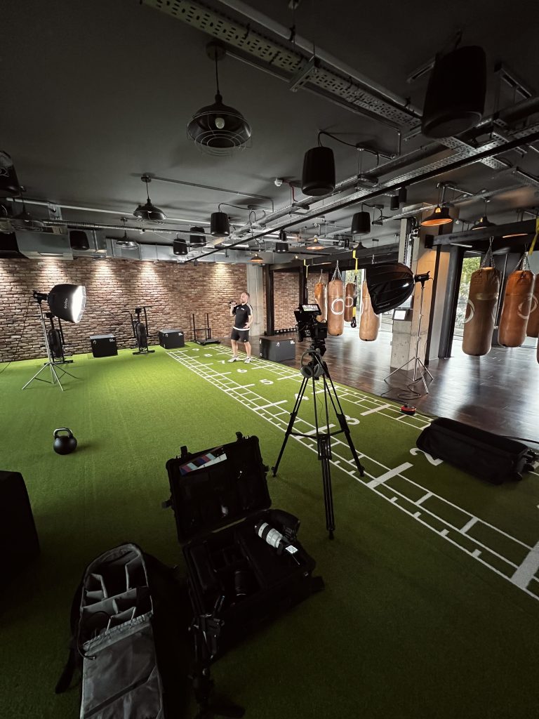 A gym room with a green astro turf flooring with video and lighting equipment set up, showcasing video production services.