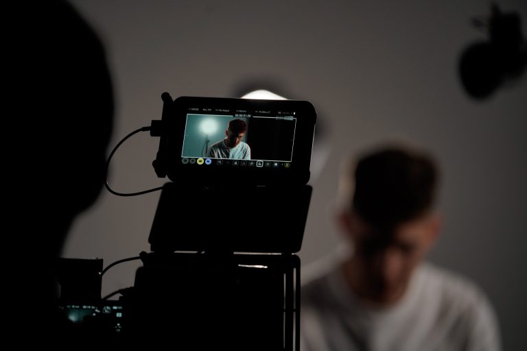 Silhouette of camera rig with a screen plugged into the camera showing the set behind which is a man with his head down Showcasing video production services