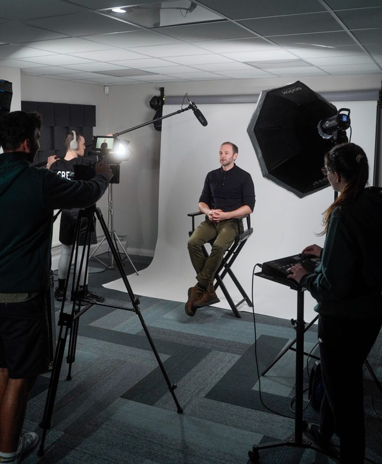 A group of people in a video production company studio with a camera and a tripod, with lighting and audio equipment, ready to capture a moment.